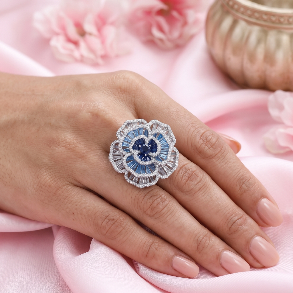 Hand wearing a decorative ring with blue gemstone on pink fabric with flowers