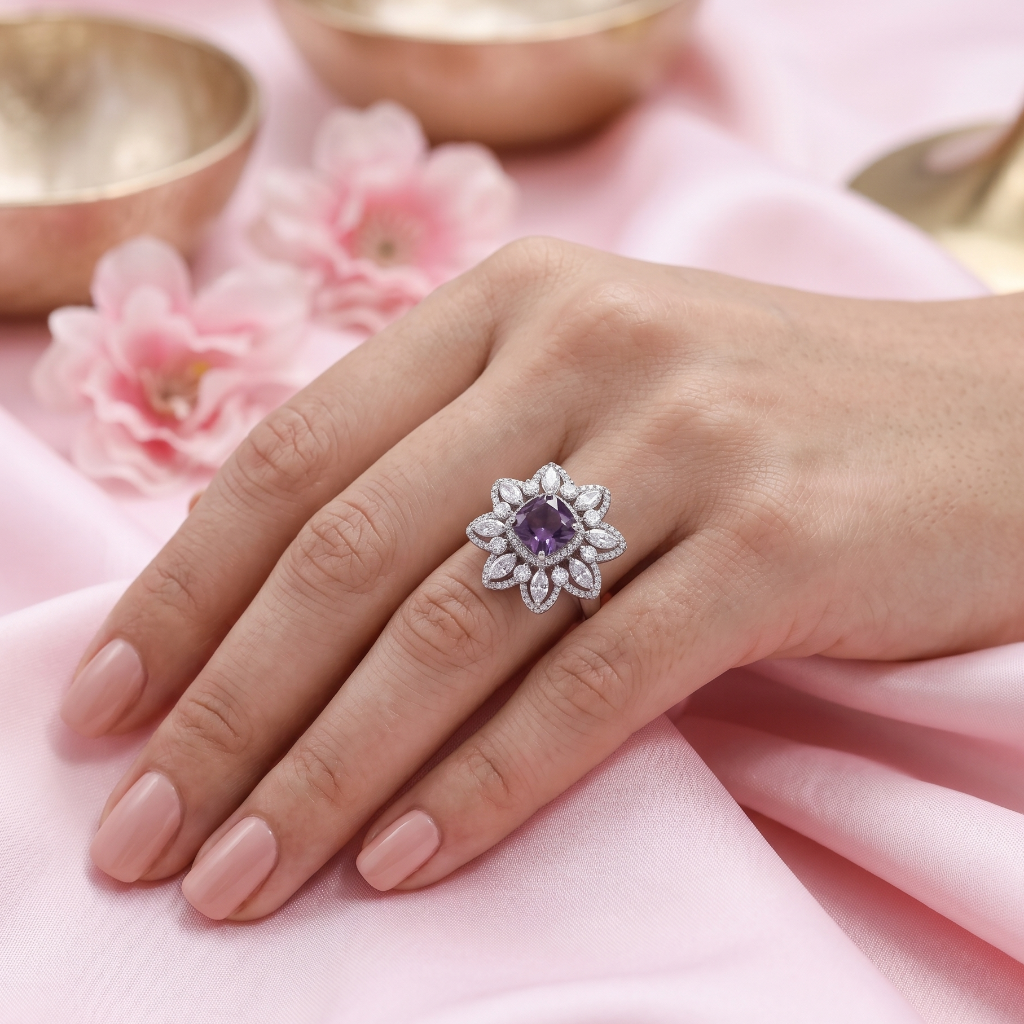 Hand wearing a decorative ring with a purple gemstone on a pink fabric background