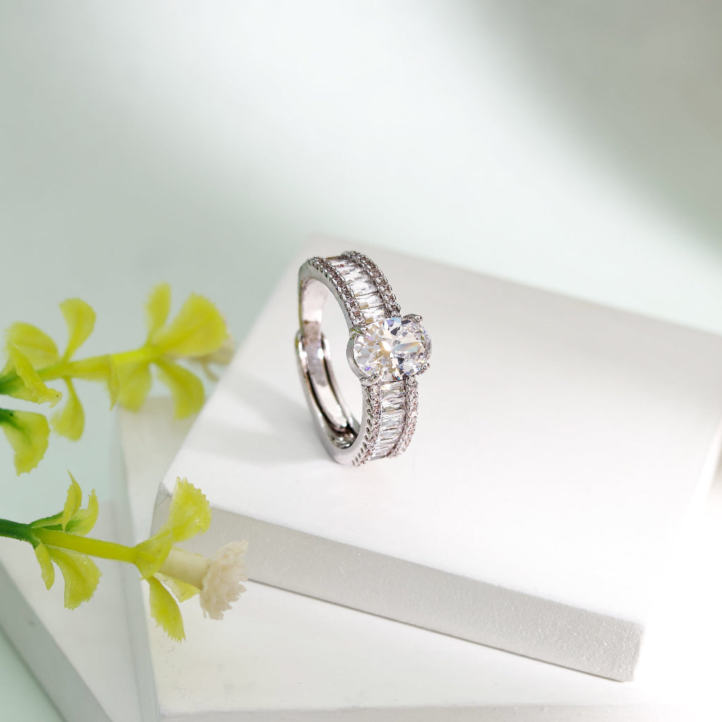 Silver ring with gemstones on a white surface with green flowers in the background